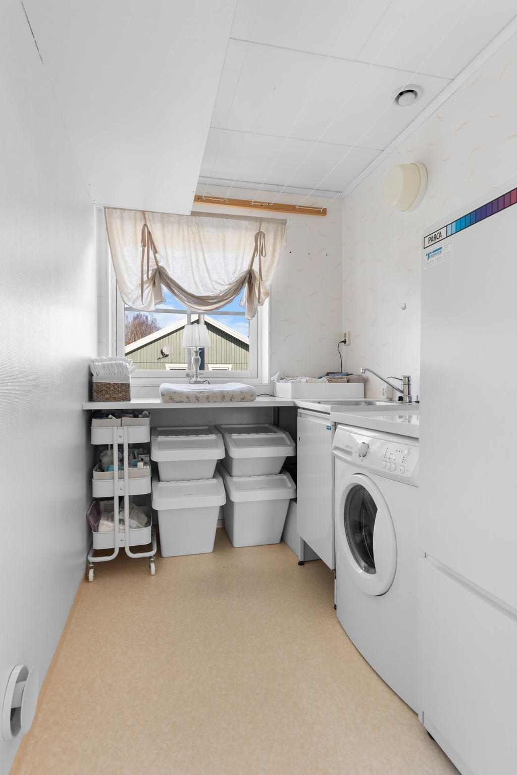 Tvättstuga med tvättmaskin, tvättbänk med ho och varmvattenberedare.