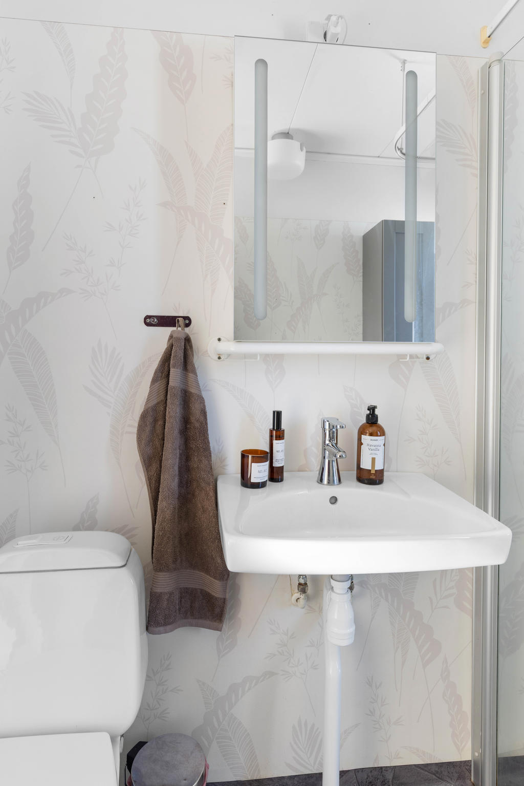 Wc, tvättställ och duschhörna med glasdörr och draperi i duschrummet