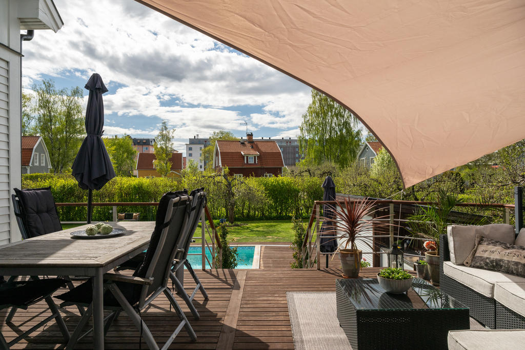 Vacker trädäckad uteplats som nås både från allrummet på entréplan och från det inbjudande poolområdet, vilket skapar en naturlig övergång mellan hus och trädgård och bjuder in till långa sommarkvällar, umgänge och avkoppling.