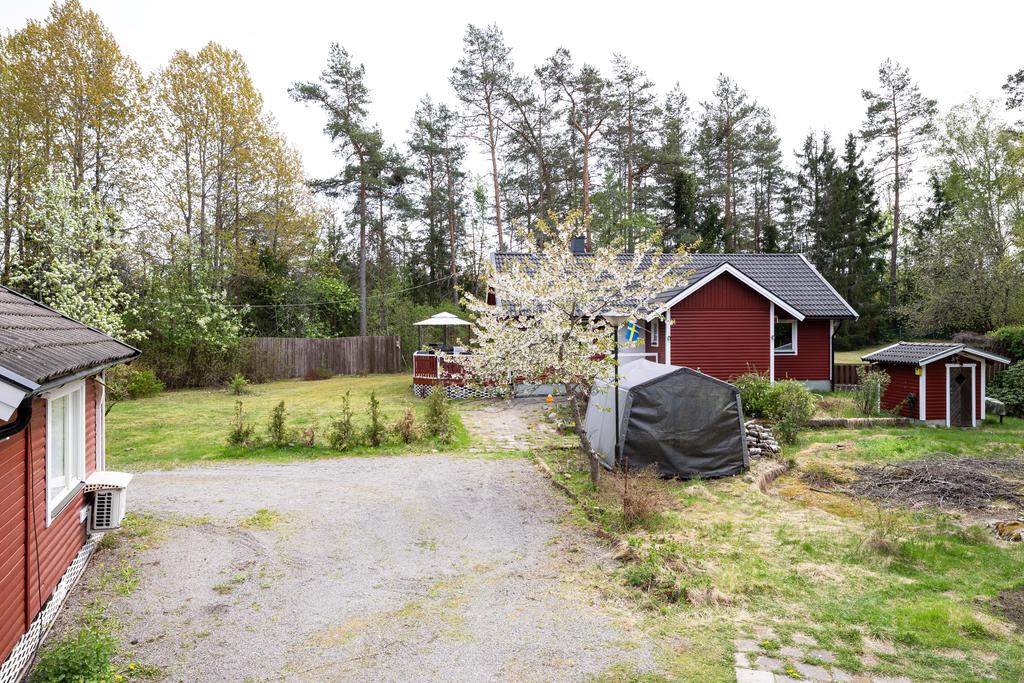 Gäststugan till vänster i bild, grusat uppfart och tomten med buskar och träd.