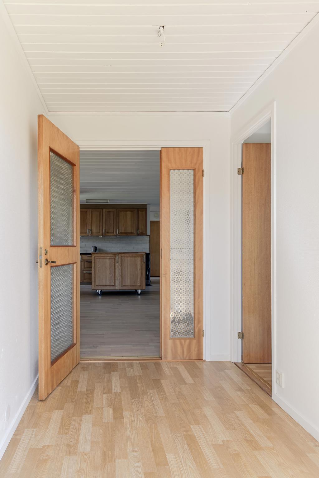 Ljus hall med parkettgolv och plats för avhängning. Härifrån nås bostadens olika rum via en praktisk planlösning.