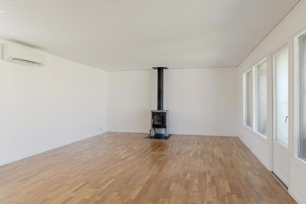 Ljust vardagsrum med stora fönsterpartier och utsikt mot trädgården. Kamin ger rummet en naturlig samlingspunkt.