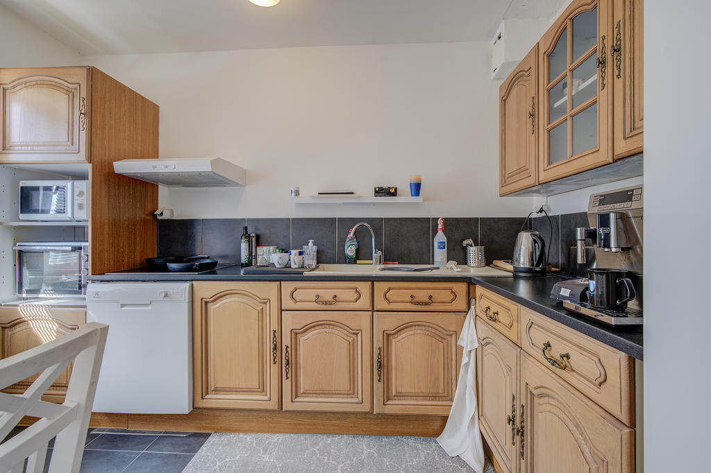 Kök med ugn, spishäll, fläkt, kombinerad kyl/frys och diskmaskin. Träfärgad skåpinredning och praktiskt klinker på golv.