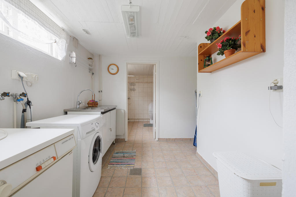 Tvättstuga med klinkergolv, utrustat med tvättmaskin samt torktumlare och tvättställ