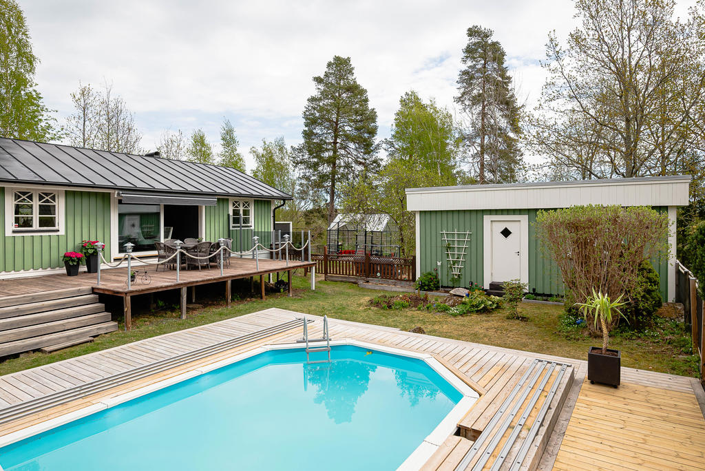 Uteplats mot poolen, växthus i bakgrunden och gäststuga