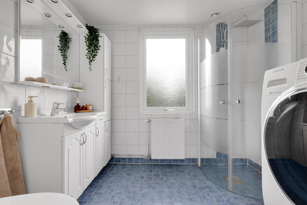 Helkaklat badrum med dusch, badrumsskåp med generös förvaring, tvättmaskin och WC samt spegelskåp med spotlights