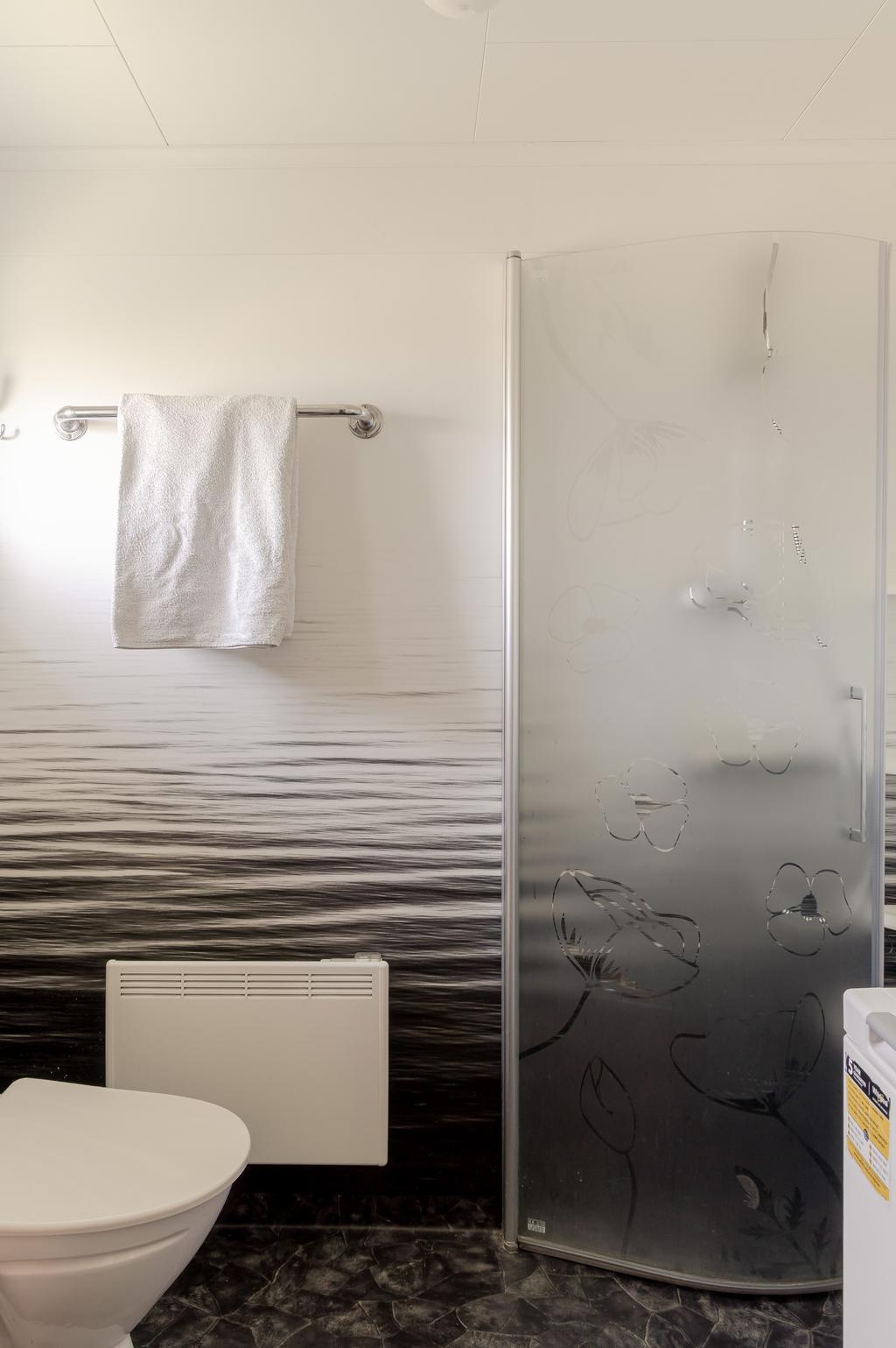 Badrum med plastmatta på golv och väggar. Här finns en duschhörna och även en tvättmaskin.