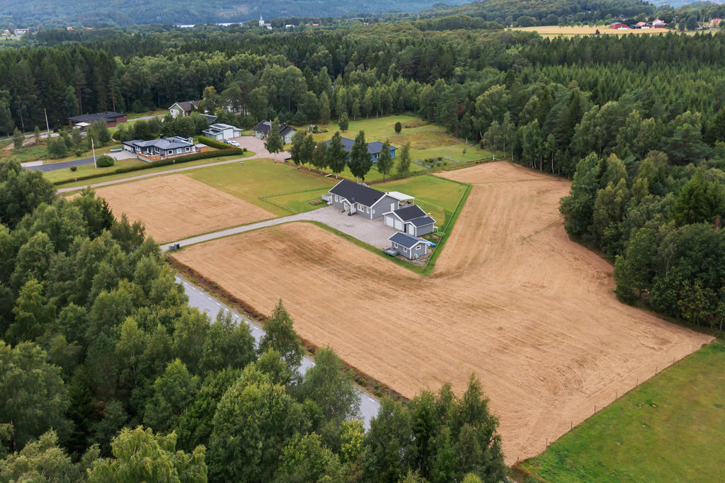 Vy över markerna med huset bakom trädraden i mitten.