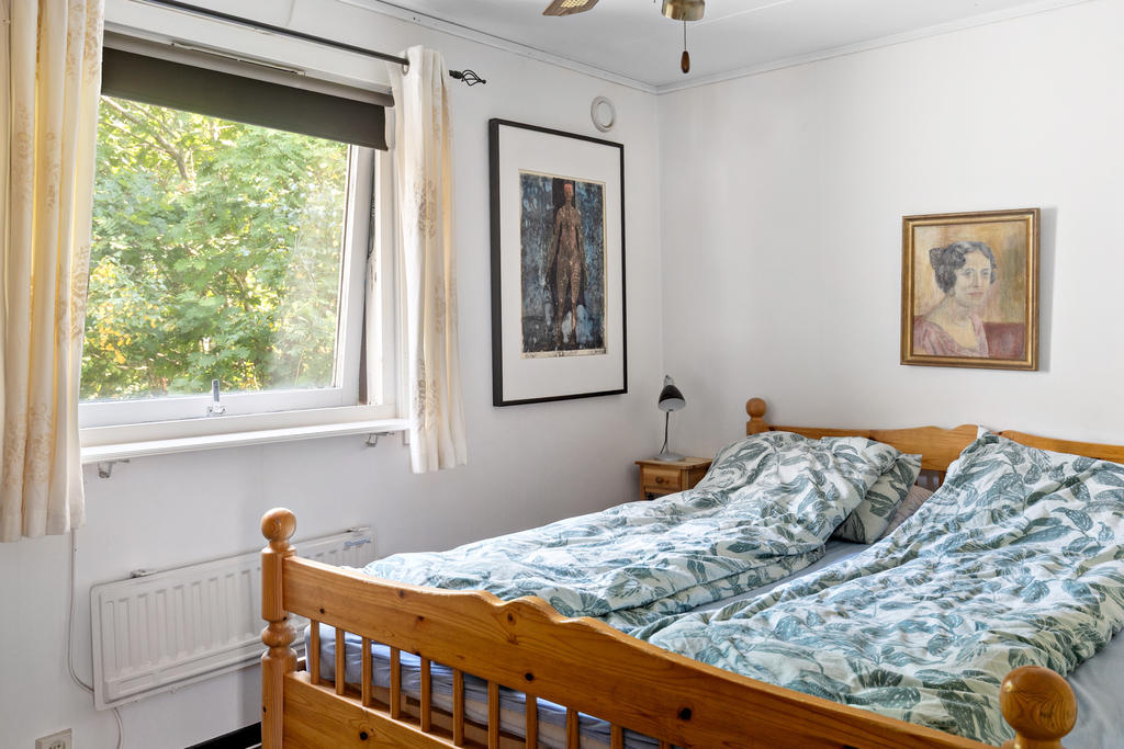 Rymligt sovrum med plats för dubbelsäng och sängbord. Det stora fönstret ger ett behagligt ljusinsläpp och utsikt mot den lummiga omgivningen, vilket skapar en lugn och avkopplande miljö.