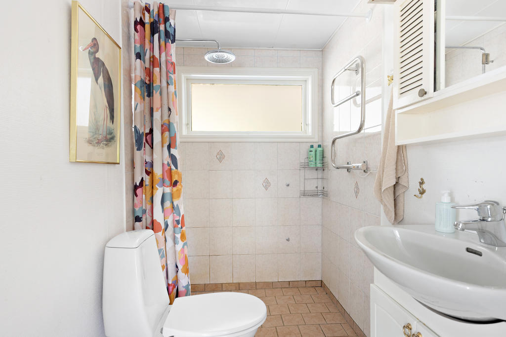 Ljust och funktionellt badrum utrustat med dusch, WC och handfat med kommod. Fönstret bidrar med naturligt ljus och god ventilation, medan handdukstorken ger extra komfort.