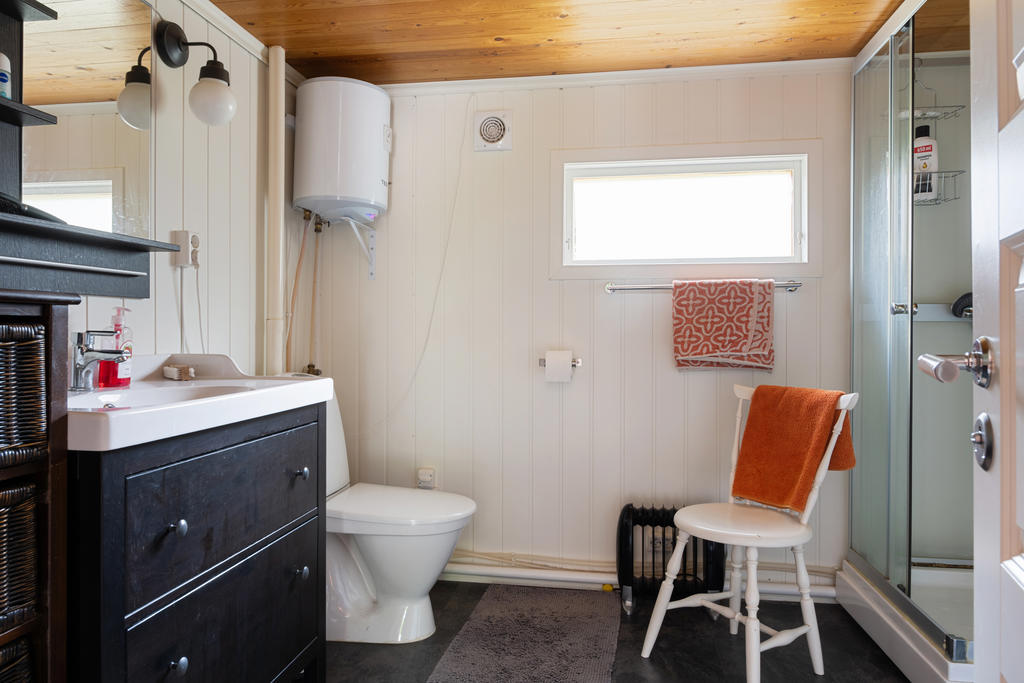 Badrum med wc, handfat med kommod, duschkabin och varmvattenberedare är placerad här. Våtrumsmatta på golvet och träpanel på väggarna.