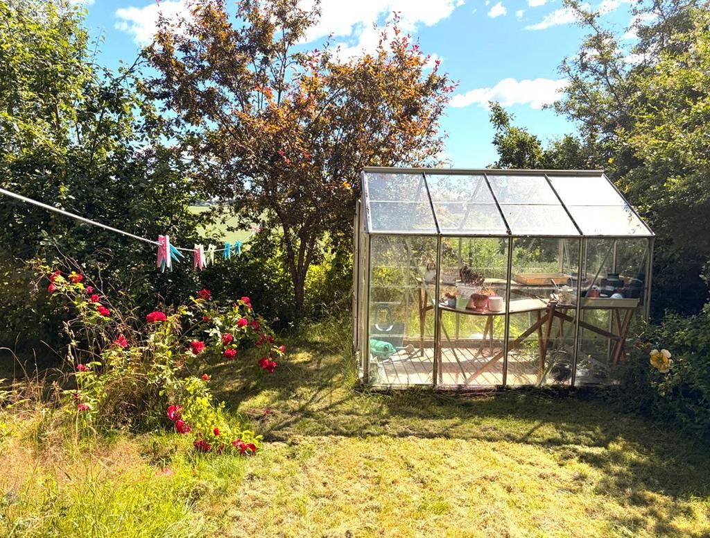Lummig trädgårdstomt med växthus och äppleträd.