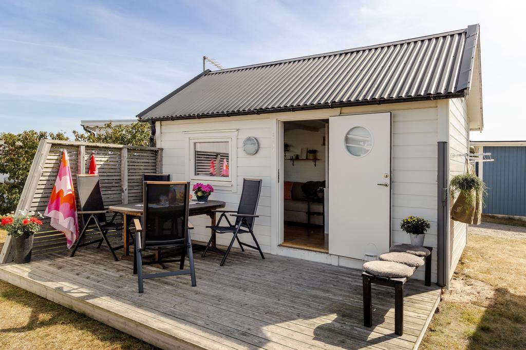 En charmig liten stuga med ljus fasad och ett trivsamt, somrigt uttryck. Här väntar ett lättskött boende med plats för både avkoppling och härliga sommardagar.