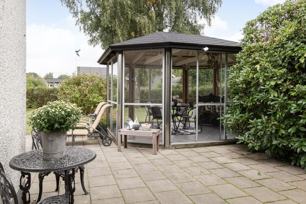 Det charmiga lusthuset blir en naturlig samlingsplats mitt i den grönskande trädgården.