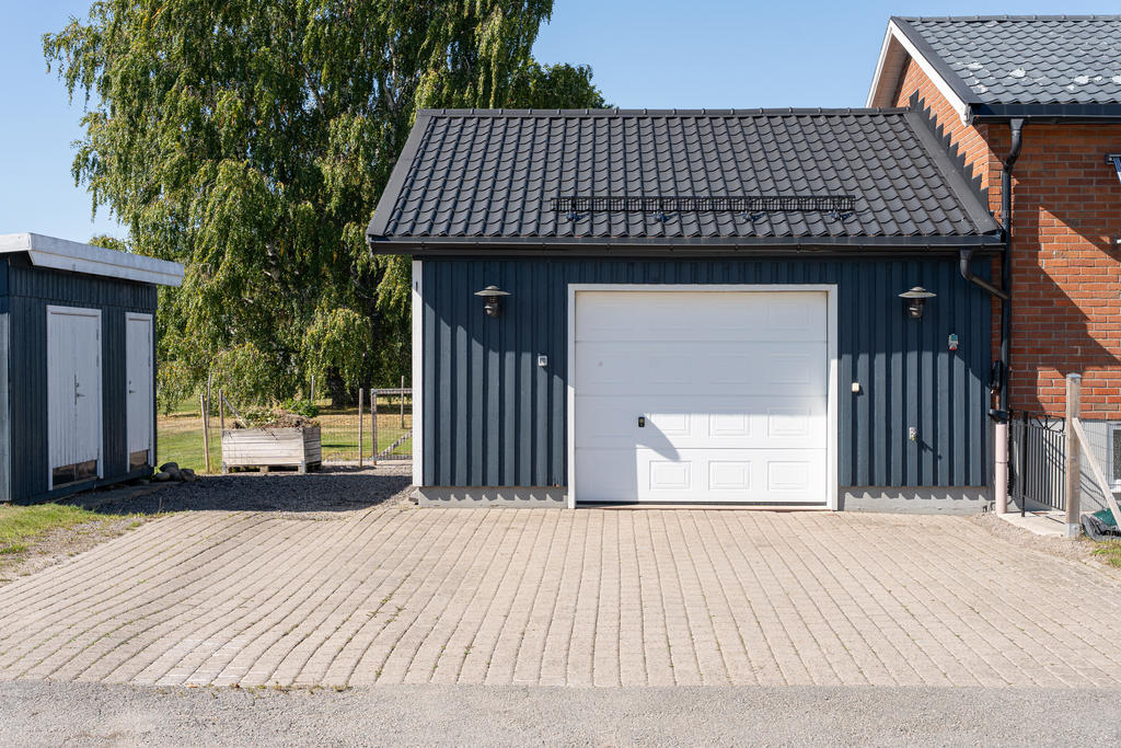 Tillbyggt garage med elektrisk port och stenlagd uppfart.