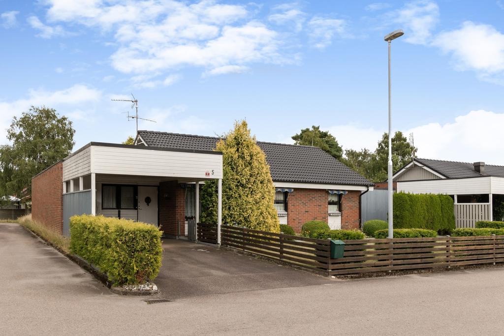 Här möts du av ett klassiskt tegelhus med praktisk parkering under tak.