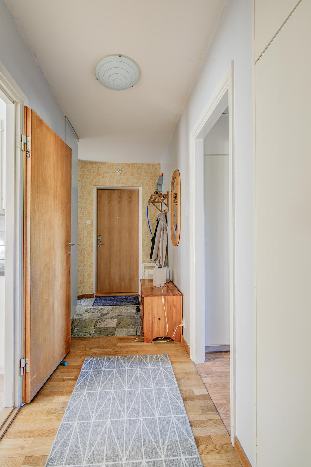 Rymlig hall med klinker och parkett på golv. Smidig förvaring i inbyggda garderober.