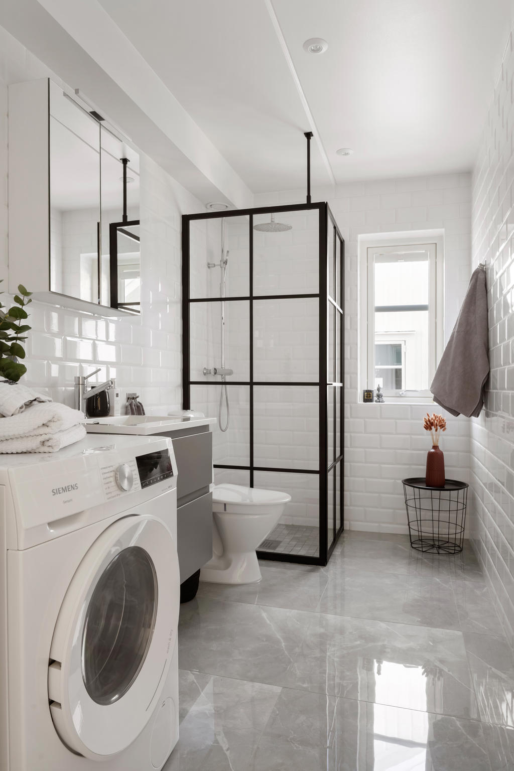 Elegant och helkaklat badrum med moderna och påkostade materialval. Den stilrena färgsättningen kombineras med svarta detaljer som ger rummet en exklusiv karaktär. Här finns en rymlig dusch med smakfulla glasväggar i svart profil, kommod med handfat, spegel och wc. Badrummet är dessutom utrustat med kombinerad tvättmaskin/torktumlare för extra bekvämlighet.