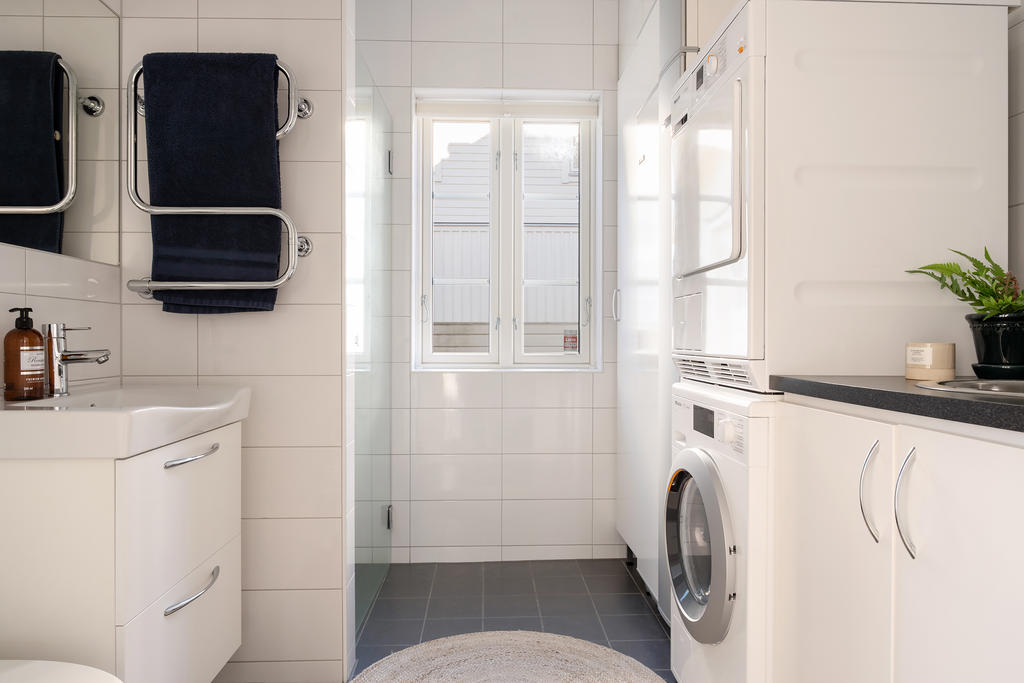 Helkaklat badrum med vita väggar och mörkgrått klinkergolv. Badrummet är utrustat med dusch med glasvägg, wc, handfat med kommod samt handdukstork. Här finns även tvättmaskin och torktumlare samt praktiska förvaringsskåp. Fönstret ger ett fint ljusinsläpp.